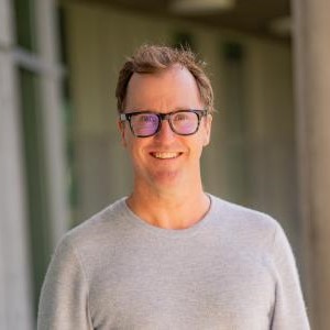 Headshot of Philip Broadbent in front of a building, wearing eyeglasses and light-colored sweater