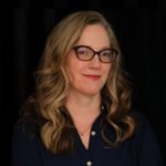 Headshot of Rebecca Davis with eyeglasses and wavy, long hair, on black background